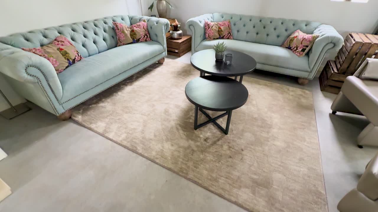 Bright modern living room with light blue tufted sofas, black coffee tables, and floral artwork