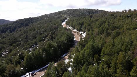 aerial push in shot of dirt road that goes through a snowy forest taken during the day