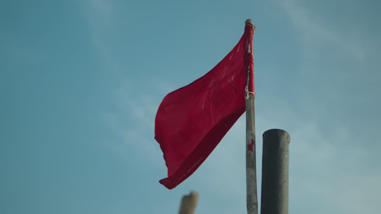 bandera roja destrozada revoloteando contra un cielo azul claro, simbolizando angustia o advertencia, disparada a la luz del día
