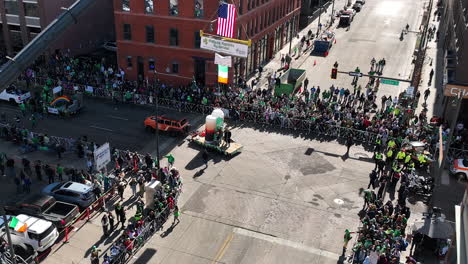 Rising-aerial-view-of-a-truck-float-driving-through-a-downtown-Saint-Patrick's-Day-parade-in-Denver,-Colorado