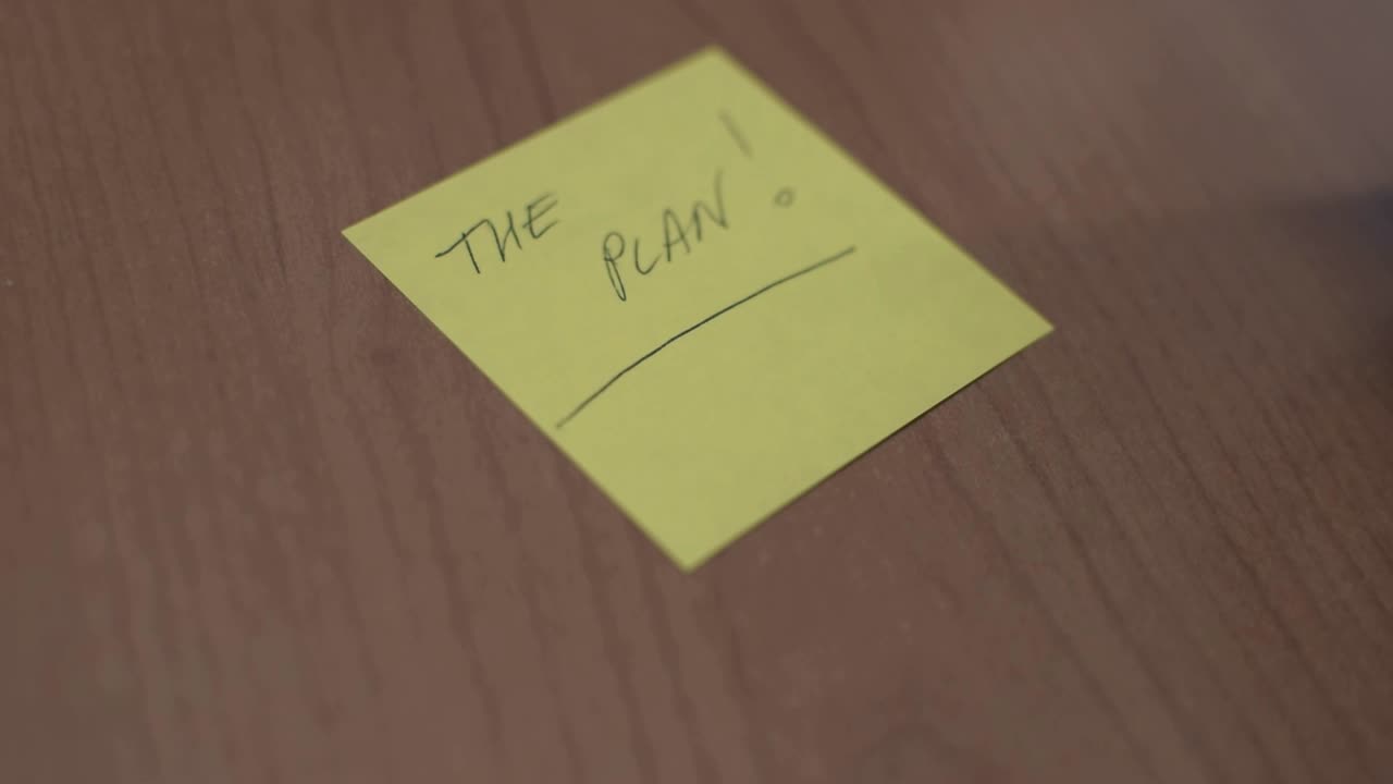 Writing on a yellow post it "The Plan