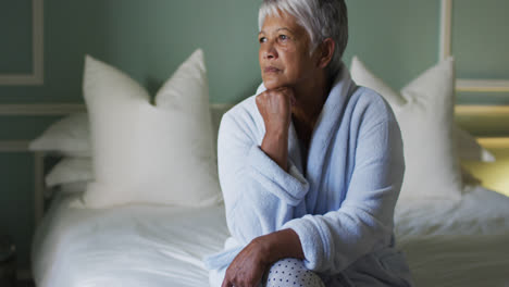 Senior-mixed-race-woman-at-home-sitting-on-bed-thinking