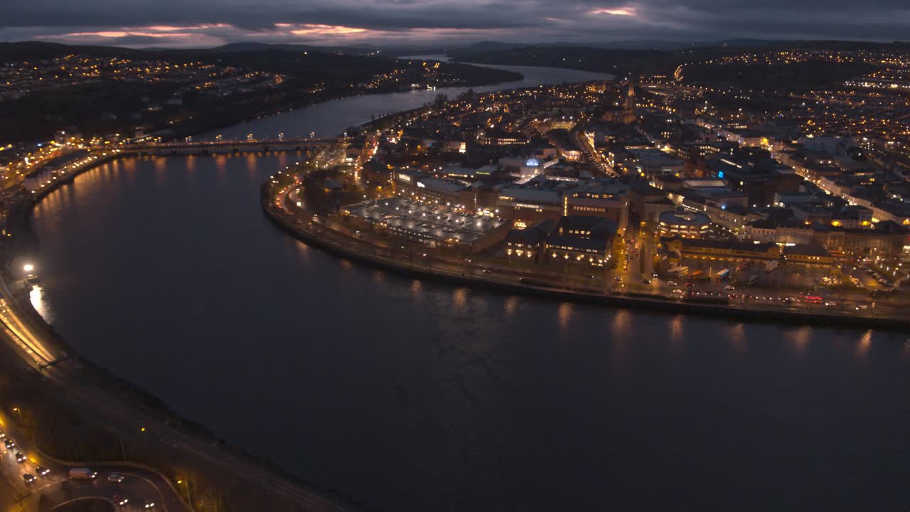 Londonderry - Derry - Stroke City - Legenderry night time aerial footage in UHD. Cityscapes of the Peace Bridge, The Foyle River, Guildhall, St Columb's Cathedral, Shipquay Street, Craigavon Bridge