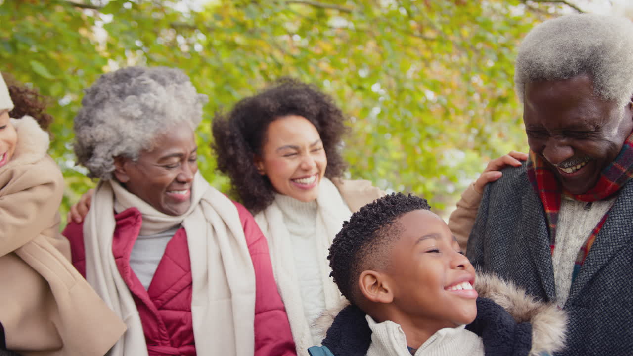 Kamera fährt entlang der Gesichter einer lächelnden Mehrgenerationenfamilie, die bei einem gemeinsamen Spaziergang durch die herbstliche Landschaft in die Kamera blickt – in Zeitlupe aufgenommen