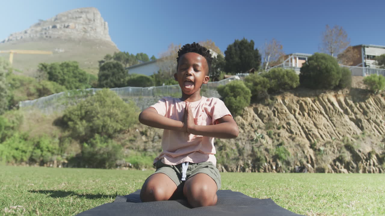Practicing yoga, boy meditating on yoga mat outdoors in school setting