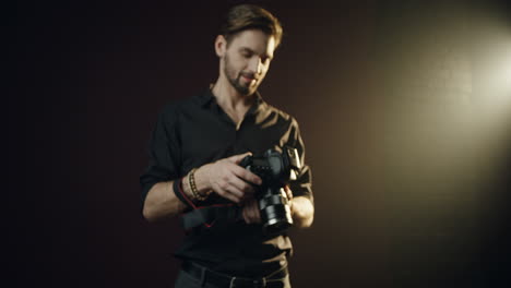 Camera-zooming-in-on-caucasian-man-photographer-who-is-holding-a-camera-and-tapping-on-it-in-darkstudio