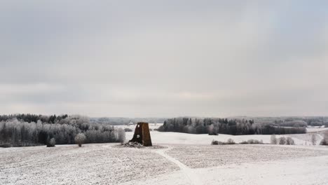 Aerial view of ancient windmill ruins on a snowy hilltop in the countryside with frozen forest in the background. Drone shot in a bright winter day.