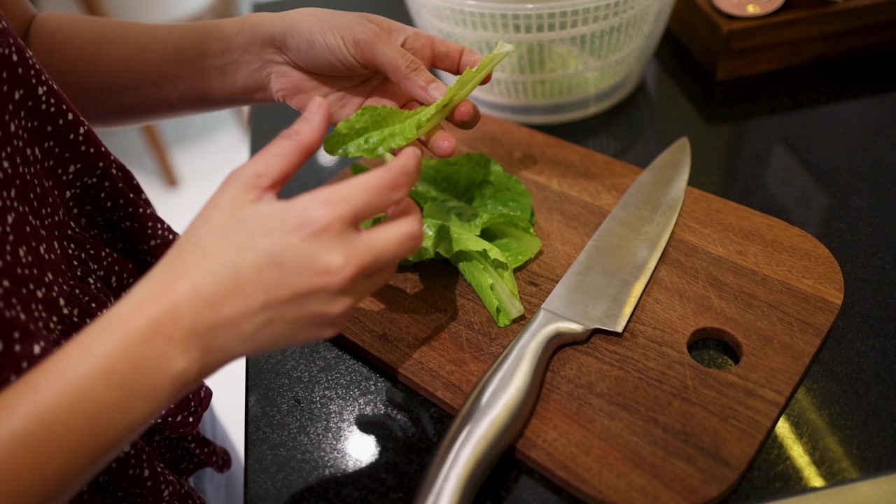 Primo piano delle mani di uno chef che sistemano foglie di lattuga verde su un tagliere di legno