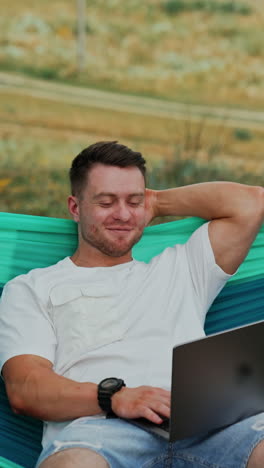 man working on laptop in a hammock outdoors