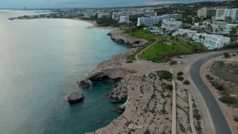 Descenso-Aéreo-Sobre-El-Puente-De-Los-Amantes-O-El-Puente-Del-Amor-En-Chipre-Al-Atardecer-Con-La-Costa-De-La-Ciudad-De-Ayia-Napa-Como-Telón-De-Fondo