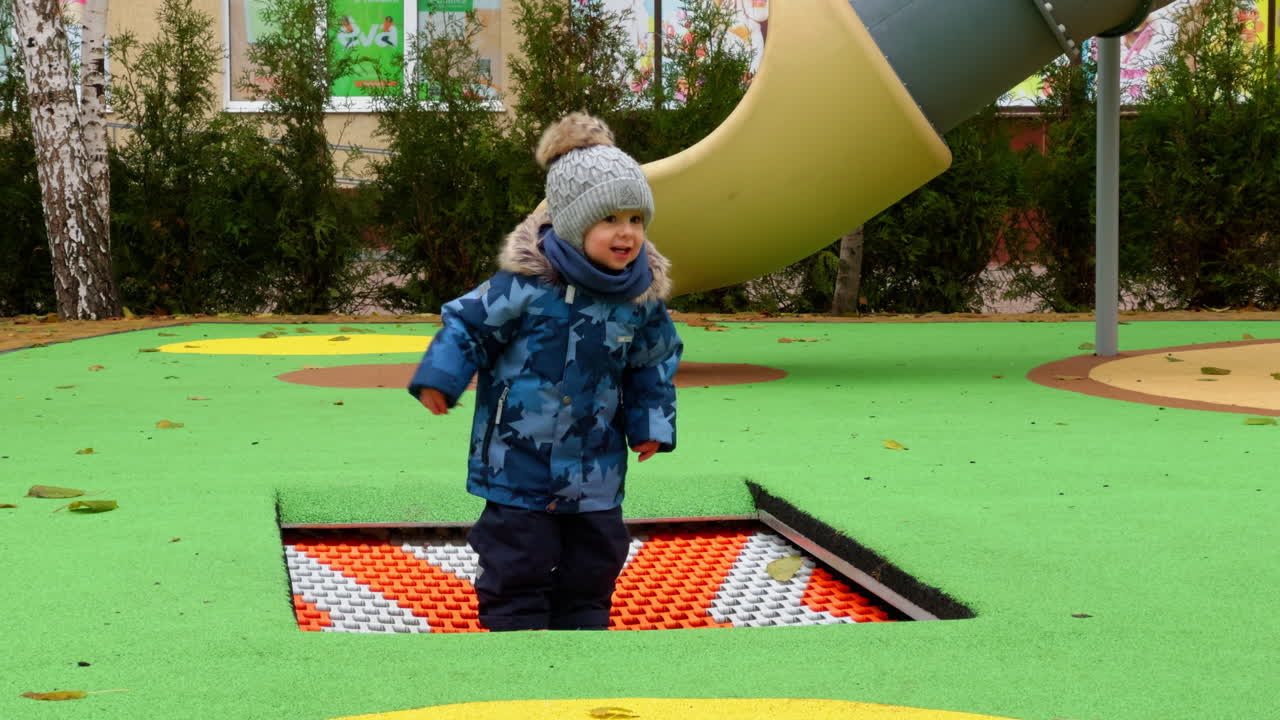 Adorable baby jumping happily on the playground trampoline. Toddler having fun time outdoors in autumn.