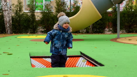 adorable baby jumping happily on the playground trampoline. toddler having fun time outdoors in autumn.