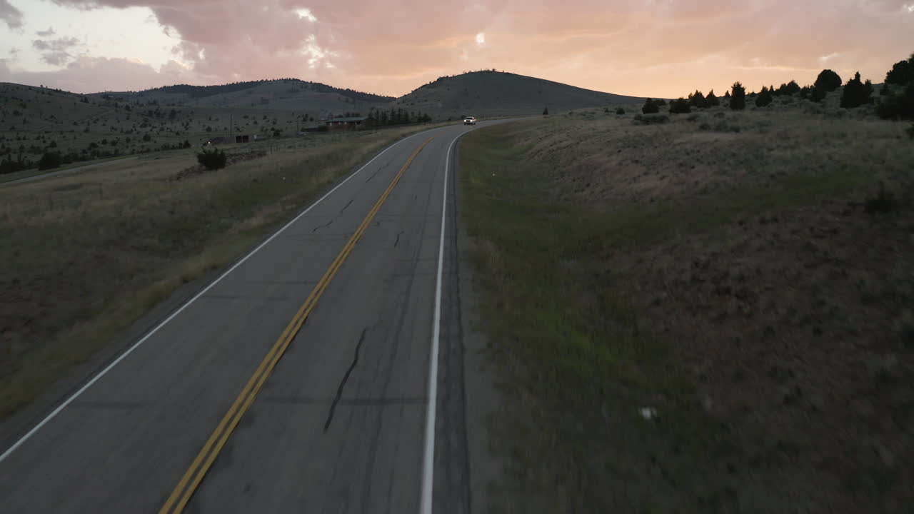 Filmagem aérea de drone com tráfego que se aproxima na Estrada do Passo da Montanha de Montana, Montana, EUA, com nuvens rosadas no horizonte