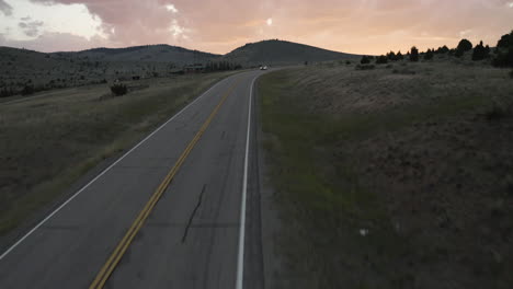 aerial fly over drone footage with oncoming traffic on montana mountain pass road, montana, usa with pink clouds in the horizon