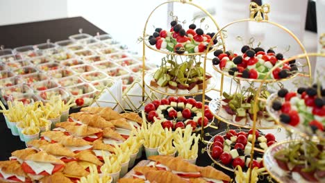 a slow dolly-in camera move pushes towards a delicious and varied catering buffet, showcasing croissant sandwiches, mini burgers, fries, and other appetizers for a special event.