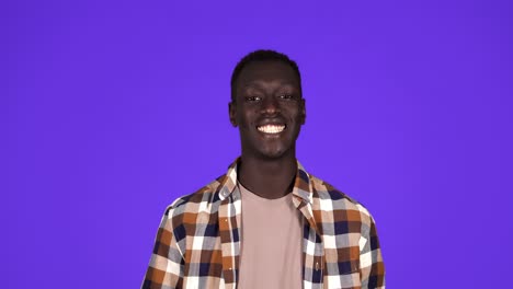 Happy-African-American-man-short-haired-in-plaid-shirt-throwing-dollars-banknotes,-wasting-money,-concept.-Isolated-over-blue-background