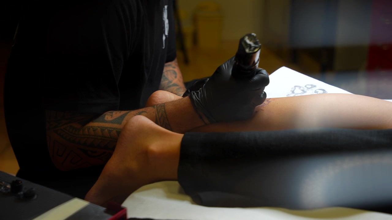 Tatuoija työskentelee asiakkaan jalalla yksityiskohtaisen sapluunan avulla studiotilassa.