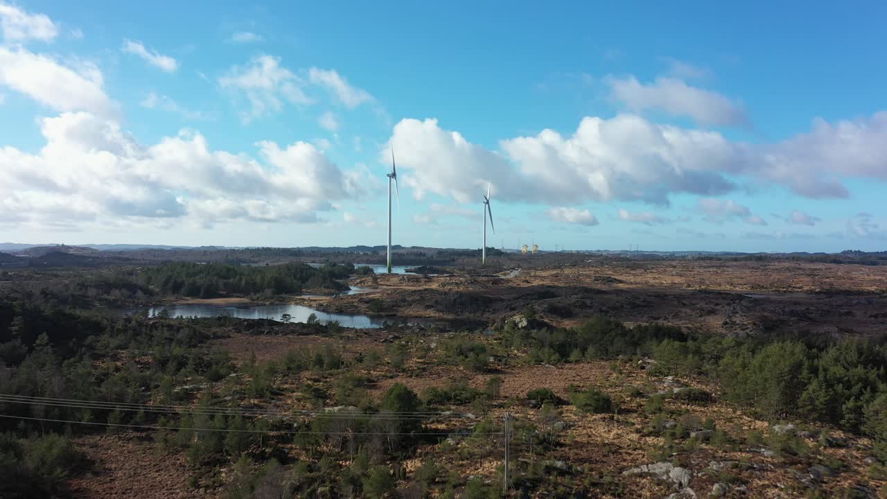 turbinas eólicas en el parque eólico de lindesnes, noruega - hermosa antena acercándose sobre las copas de los árboles con dos turbinas eólicas en el centro y reflejos del cielo en el lago - una turbina en funcionamiento y otra parada