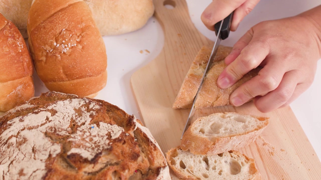 Primo piano di mani che usano un coltello per affettare una baguette croccante su un tagliere di legno