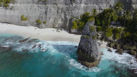 Diamond-beach-in-Nusa-Penida-with-large-rock-pinnacle-on-sunny-day,-aerial