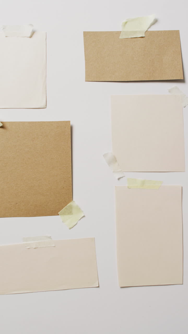 Vertical video of close up of multiple pieces of paper taped to white background with copy space