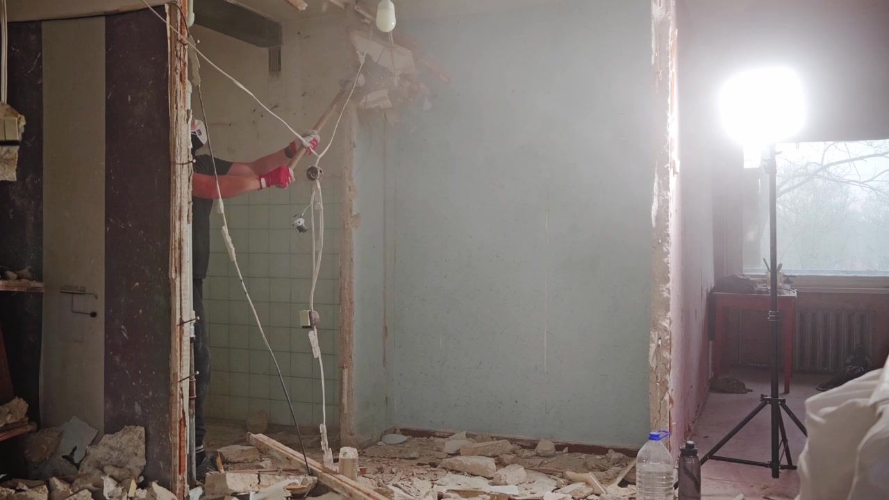 Un'inquadratura fissa cattura la demolizione di un muro mentre i detriti volano durante i lavori di ristrutturazione