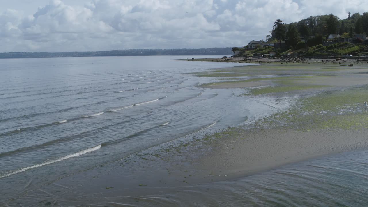 Nærbilde av droneopptak fra luften av bølgene i Dumas Bay som skyller over den gjørmete stranden.