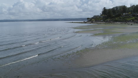 close aerial drone footage of the waves of dumas bay washing across the muddy beach of the shore.