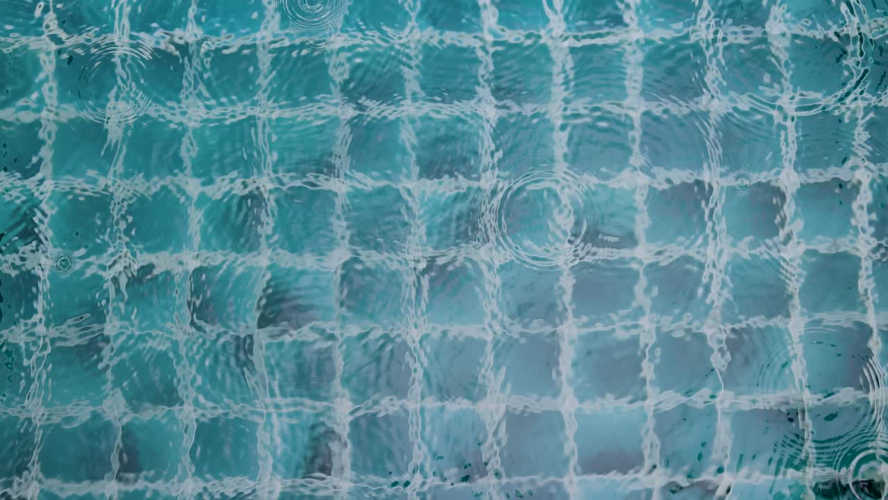 Raindrops create ripples on a tiled pool surface, capturing a serene and rhythmic natural scene
