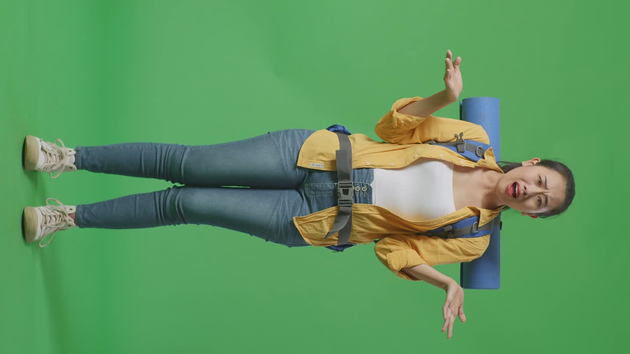 Full Body Of Puzzled Asian Female Hiker With Mountaineering Backpack Making Gestures Doubtfully And Saying Why While Standing On Green Screen Background In The Studio