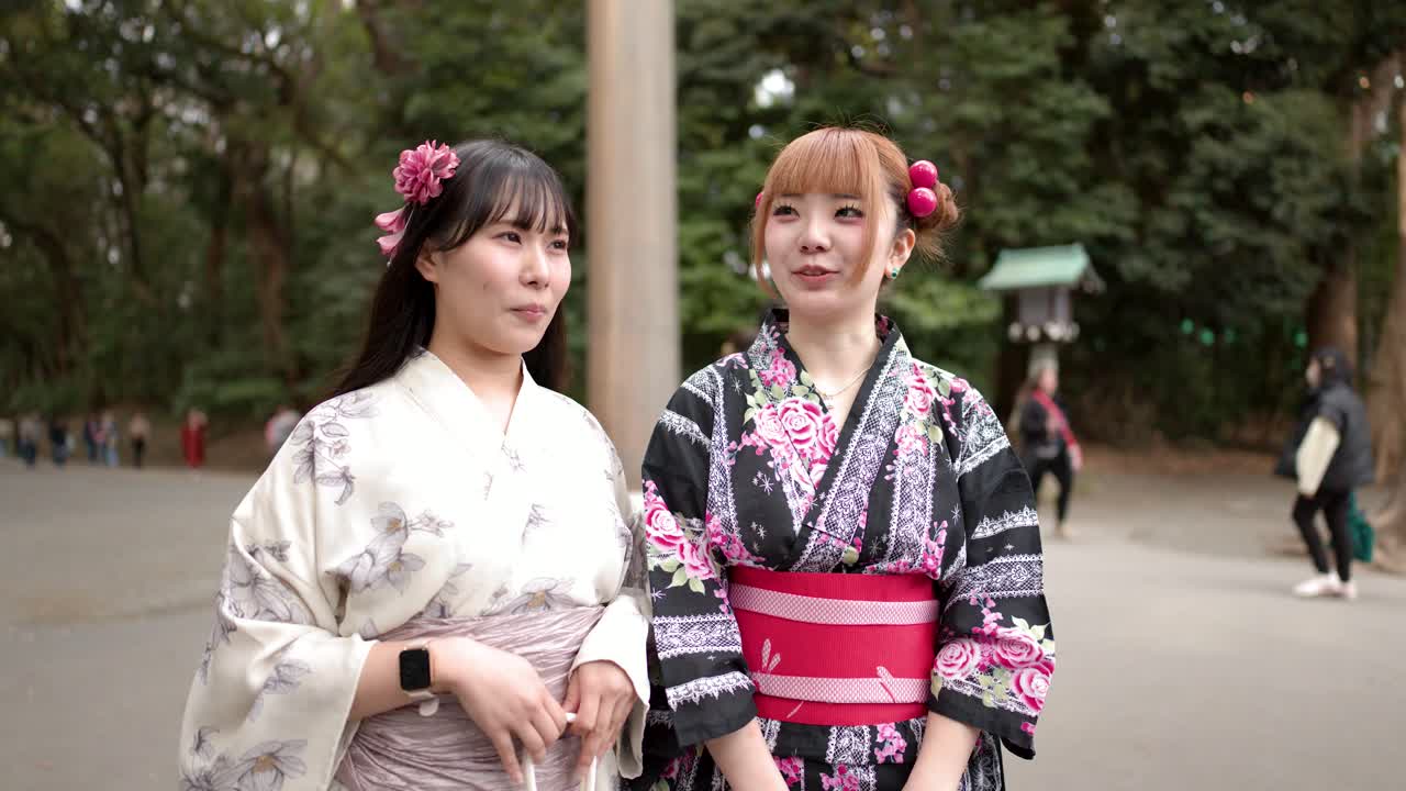 Due donne indossano yukata floreali mentre stanno all'aperto presso un santuario storico giapponese a Tokyo.
