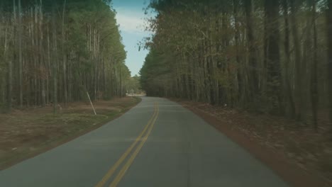 Driving-down-a-lonely-back-road-through-autumn-trees,-up-to-a-stop-sign