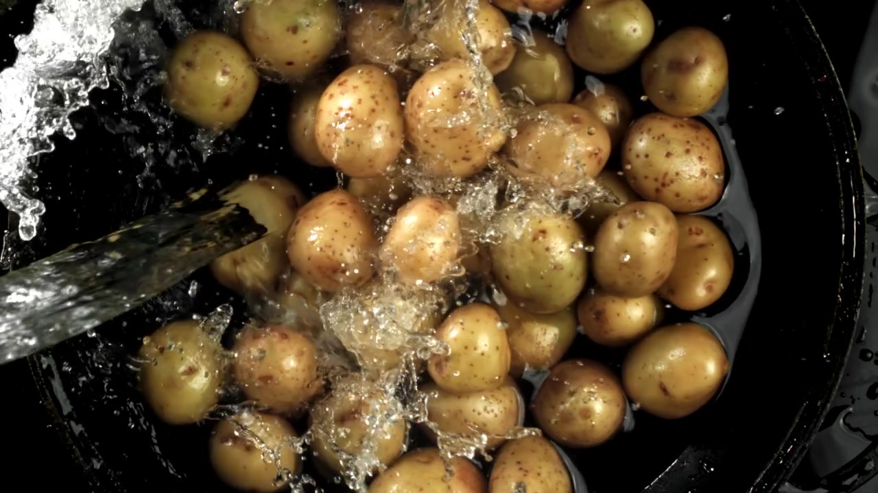 Lavaggio di patate fresche in una pentola nera con schizzi d'acqua