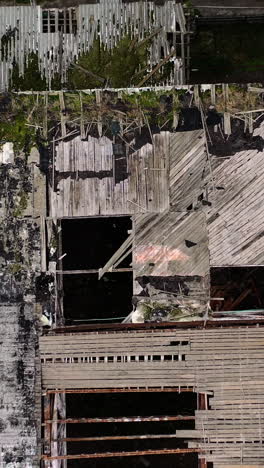 damaged roof of a building during military action. abandoned building with many holes outdoors. top aerial view. camera rising up. vertical video