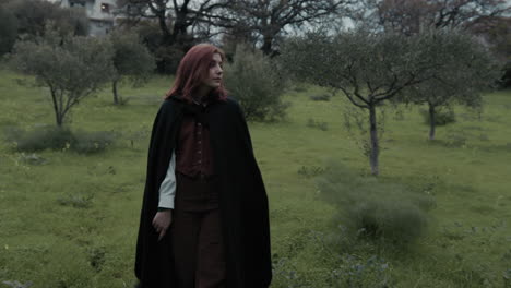 mysterious young woman walks on the meadow among olive trees in overcast evening