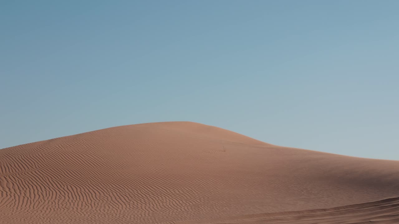 Sand dunes with rippled wave texture pattern as grains of sand are blown in dry mist over edge