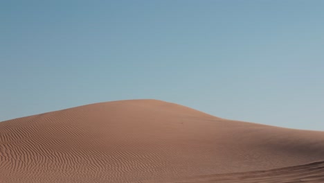 Sand-dunes-with-rippled-wave-texture-pattern-as-grains-of-sand-are-blown-in-dry-mist-over-edge