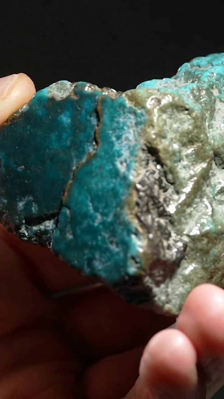 Vertikal video: Hænder løfter og roterer turkis mineral tæt på for at vise revne og metallisk plet.