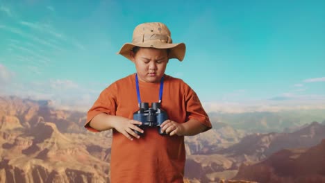 asian boy with a hat having a headache after looking through the binoculars. boy researcher examines something while traveling at the top of mountain, travel tourism adventure concept