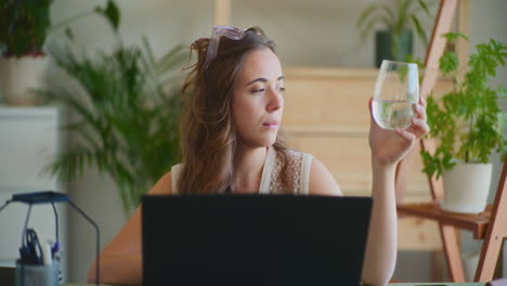 Mujer-Inspirada-Sosteniendo-Un-Vaso-De-Agua-Trabajando-En-La-Ventana-Del-Portátil.