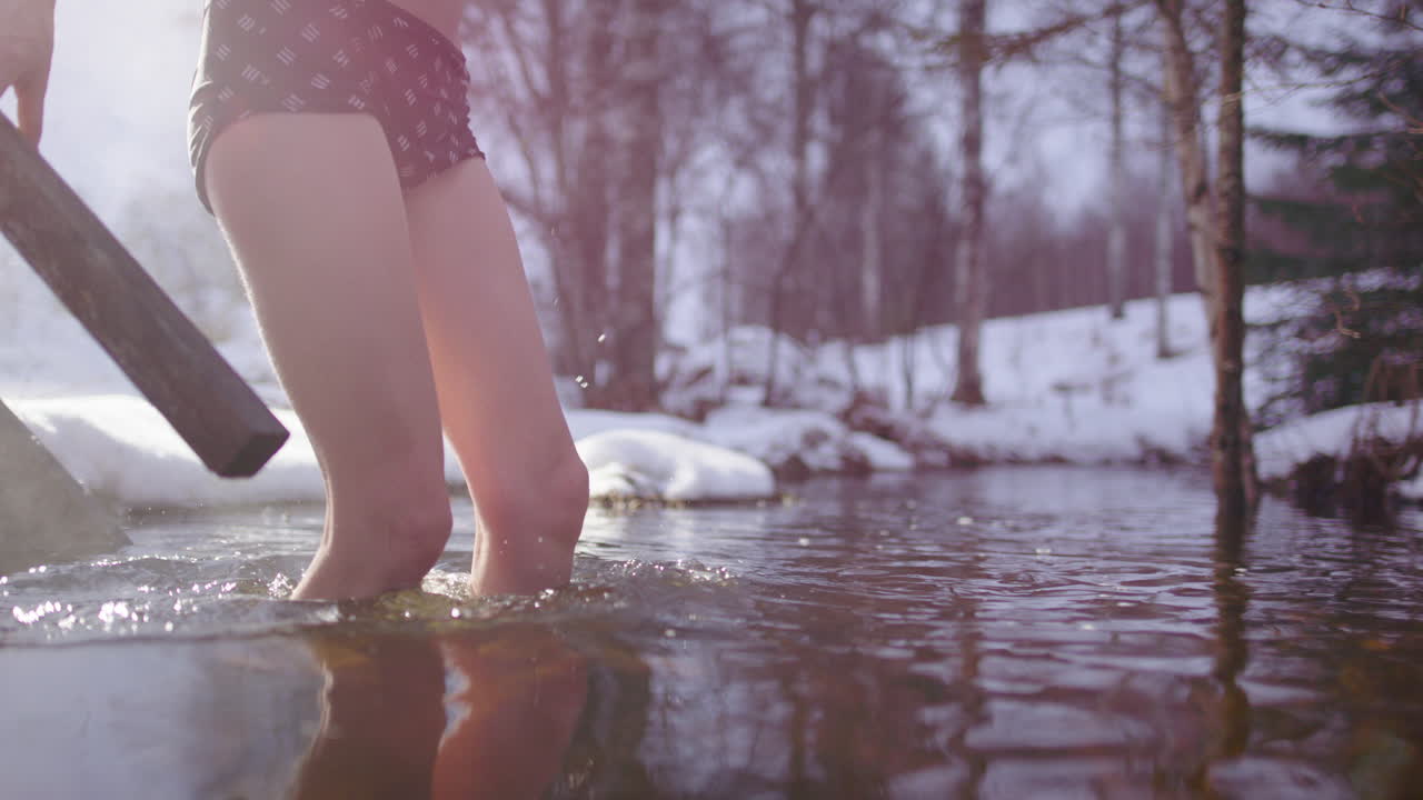 Scandinavian woman steaming hot from sauna plunge into river in snowy woods