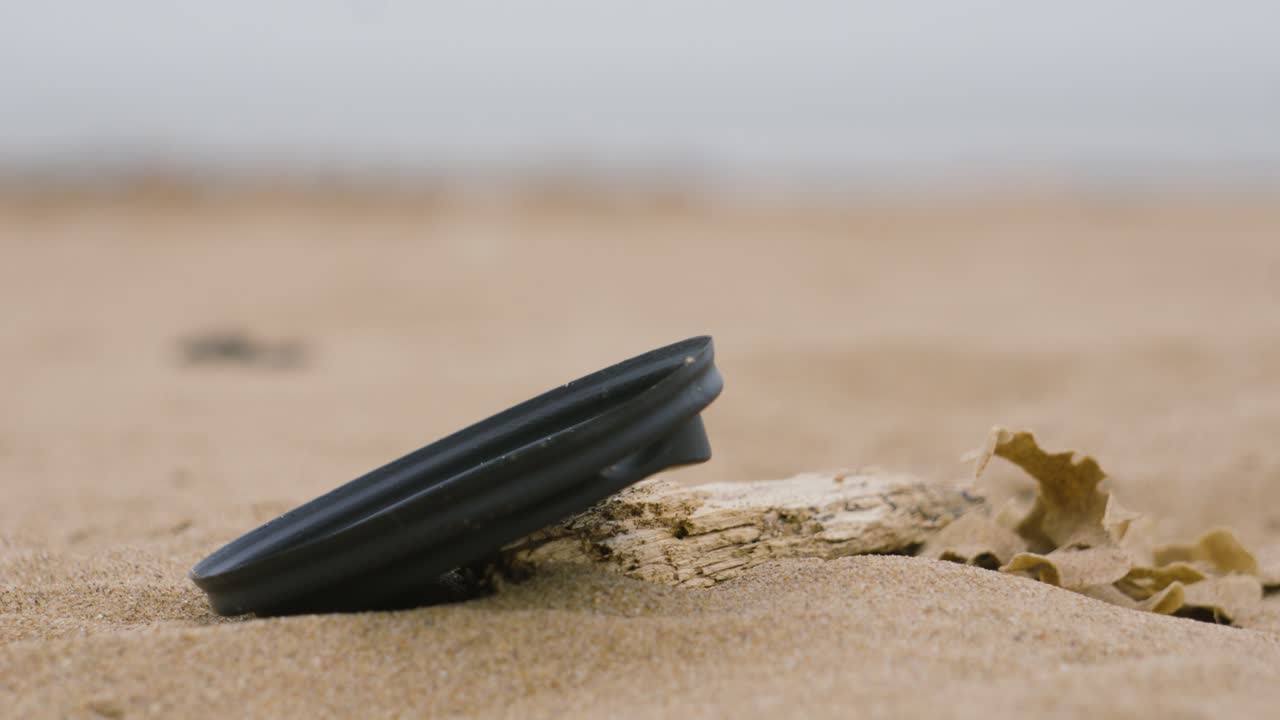 Plastic Coffee Lid Lying on Drift Wood on Sand Beach After Being Littered Causing Pollution and Potential Danger to Marine Environment