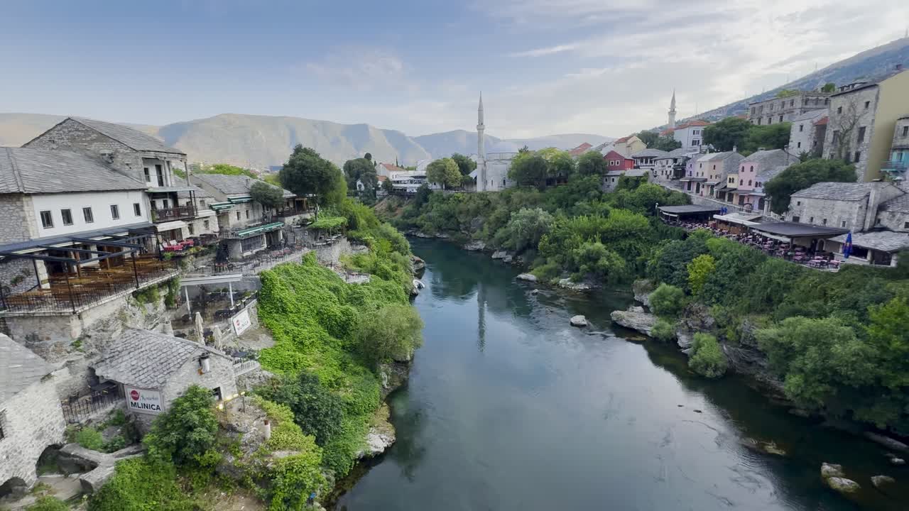Wide-angle view of Mostar Riverside with beautiful stone buildings, mosques, greenery and mountains in the background on a wonderful sunny morning; taken from Mostar Bridge - Bosnia and Herzegovina