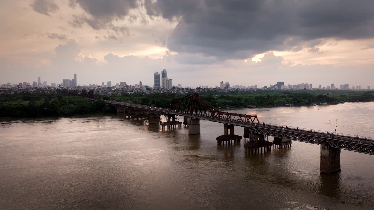 Long Bien bridge traffic with Hanoi city skylines in background under sunset sky, Drone shot