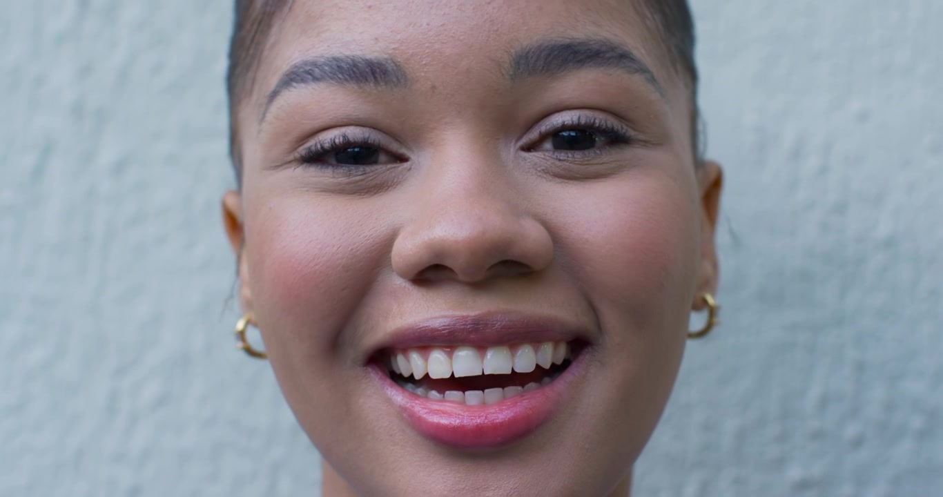 Adult African American woman on camera closeup talking laughing gold hoops lipstick textured wall