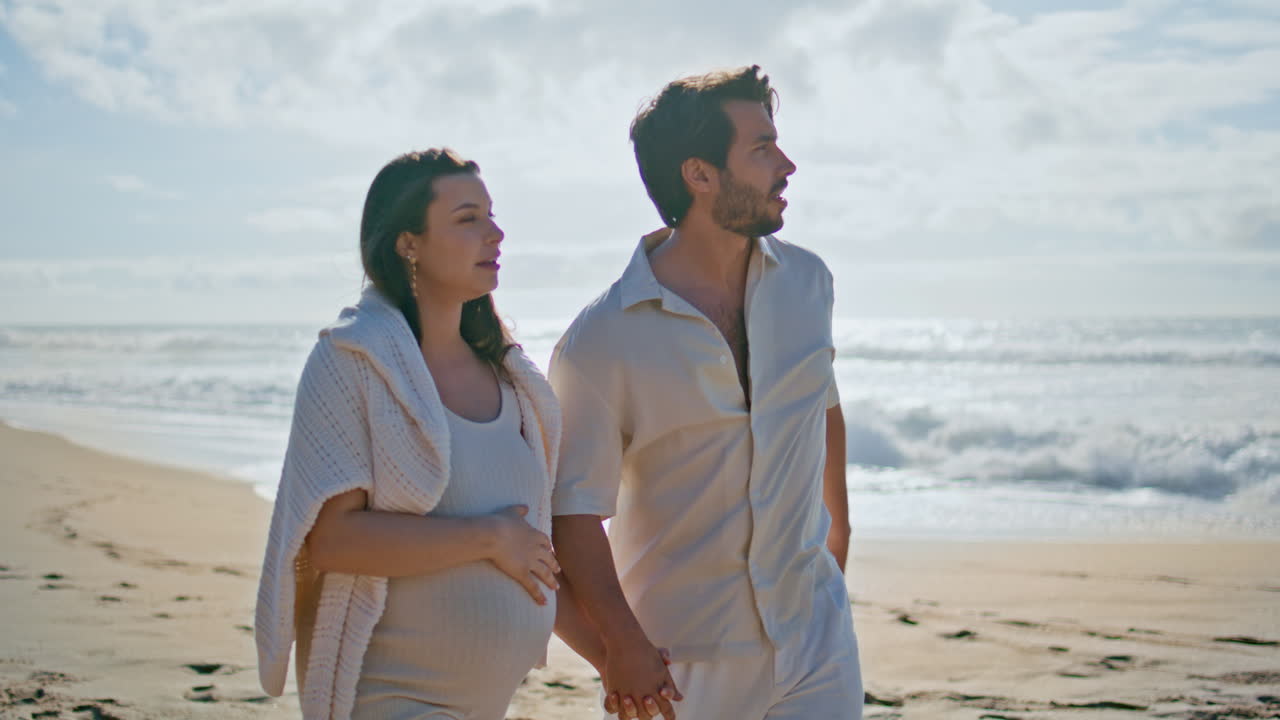 임신 한 부부는 바다 풍경을 즐기고 산책 해변 모래. 아기를 기대하는 여성