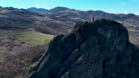 aerial footage of pietra perduca, volcanic rock, church set at top stone immersed in countryside landscape, cultivated land in val trebbia bobbio, emilia romagna, italy