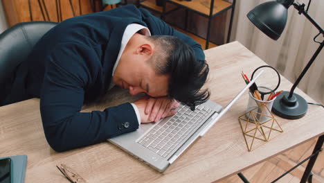 bored sleepy business man worker working on laptop leaning on hands falling asleep at office desk