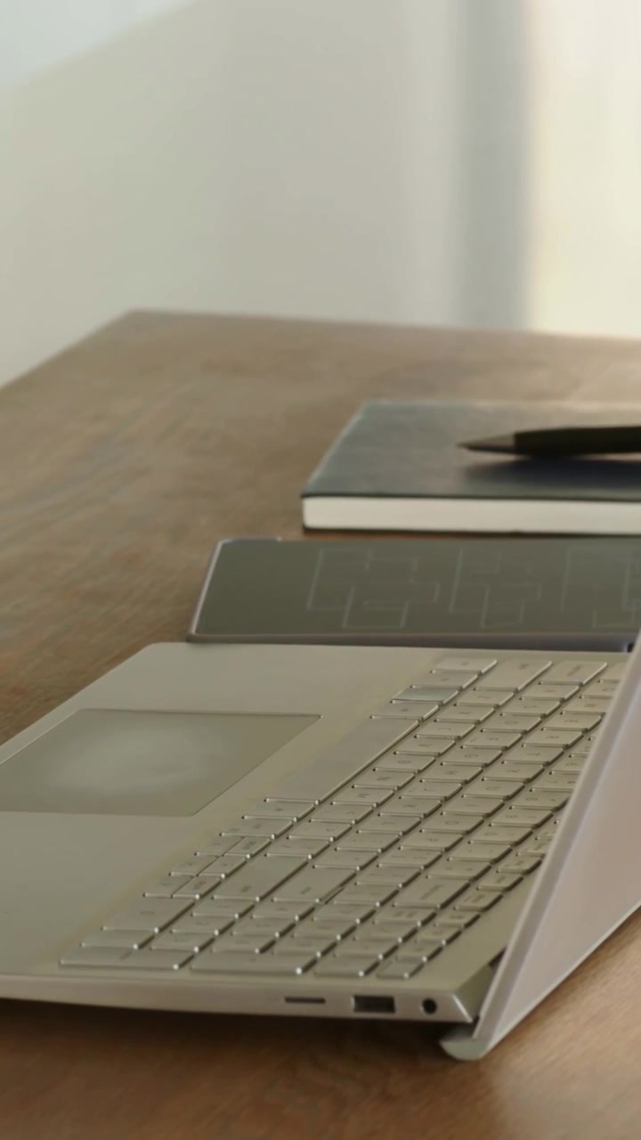 Vertical video: Panning camera across silver laptop on stand at home, showing notebook pen tablet
