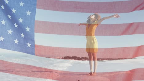 american flag waving against african american woman standing with arms wide open on the beach